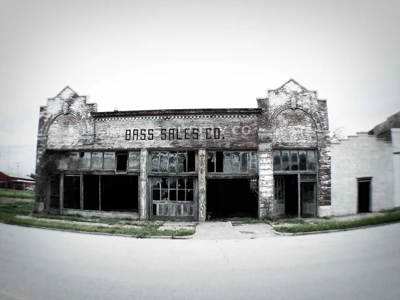Old shop facade with broken display windows, in black and white.