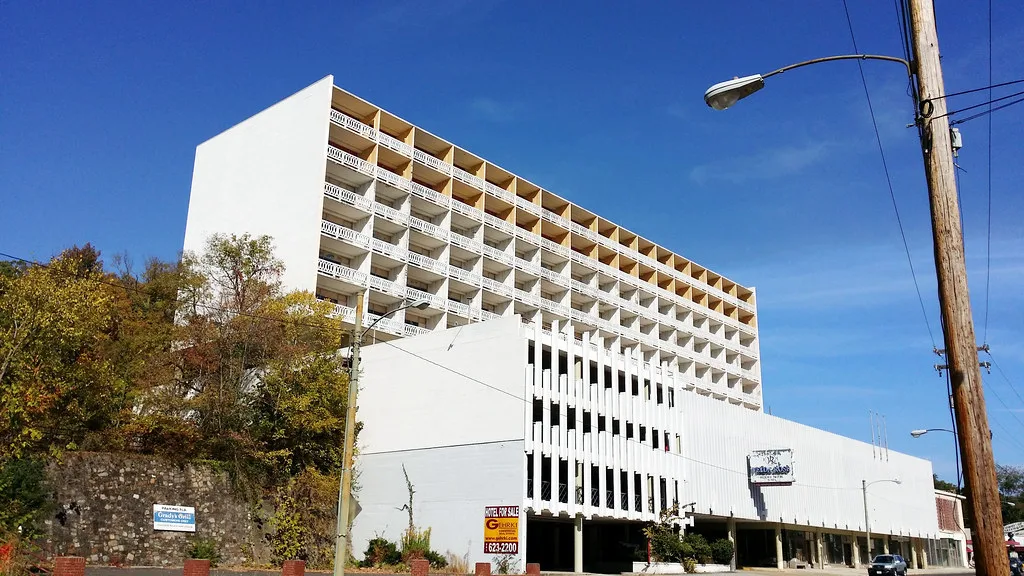 Ancien hôtel blanc à balcons devant une parcelle herbeuse.