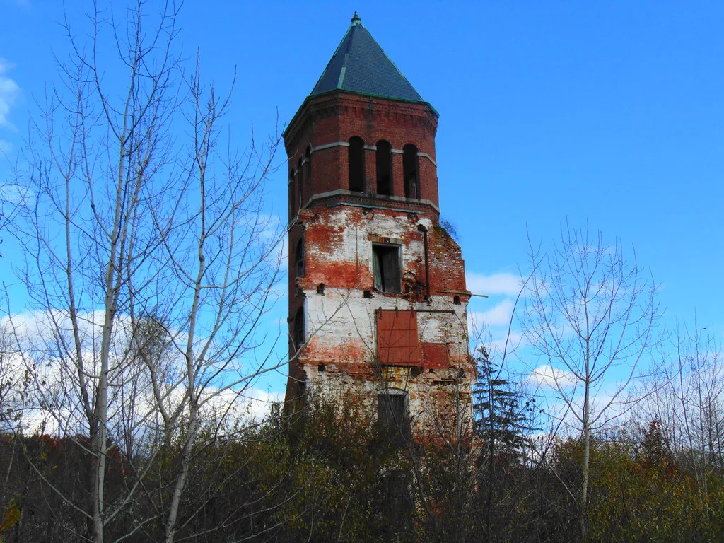 Dilapidated old brick tower among leafless trees.