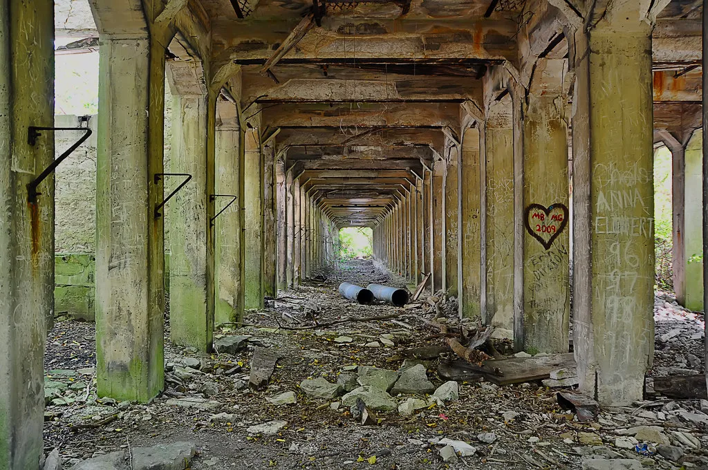 Row of deteriorated concrete pillars in a rubble-filled hall.