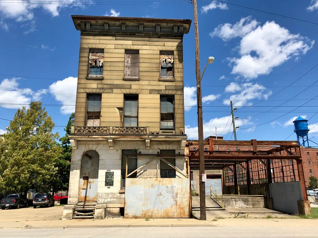 Narrow building with boarded windows beside a metal frame.