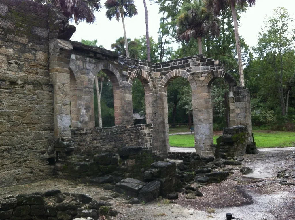 Ruined stone walls and arches of an old sugar mill among palms.