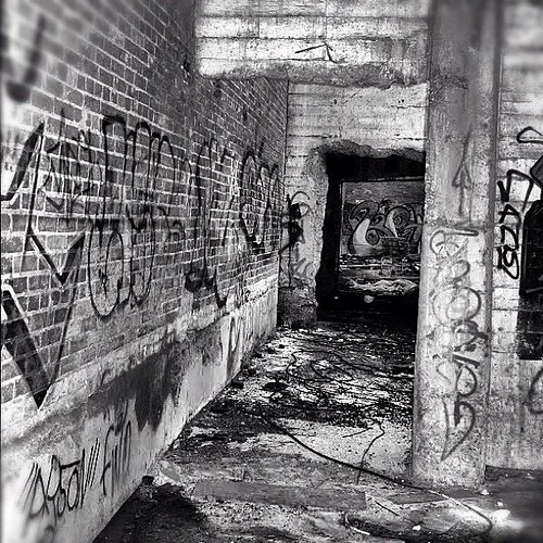 Brick and concrete corridor covered in graffiti and rubble, in black and white.