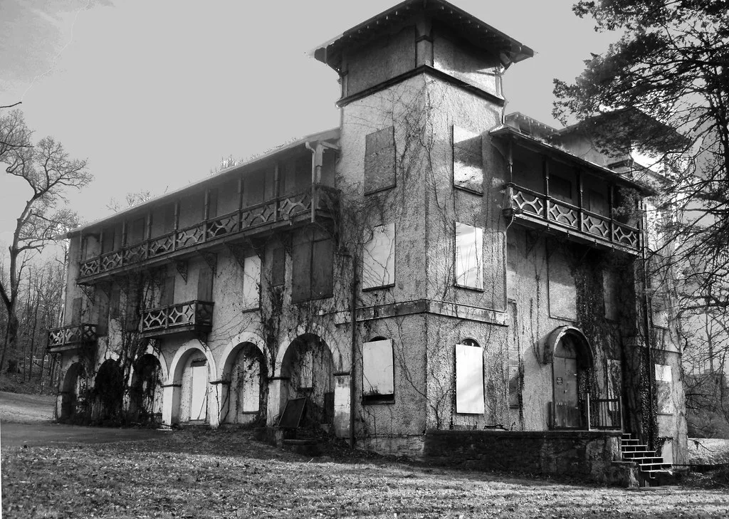 Abandoned building with a square tower and wooden balconies, boarded windows and vine-covered walls.