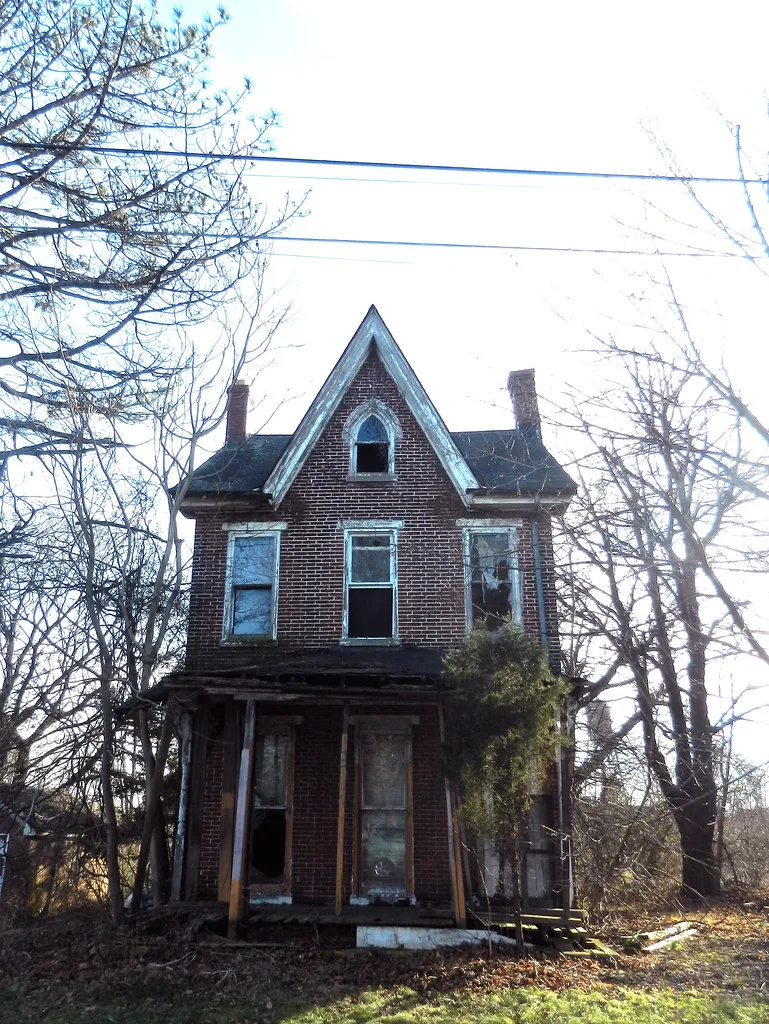 Abandoned brick house with a pointed gable and a dilapidated porch.