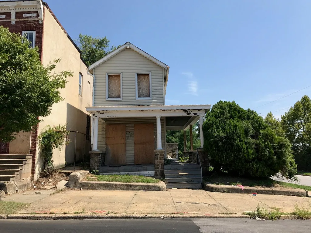 Petite maison aux portes et fenêtres condamnées, avec porche détérioré.
