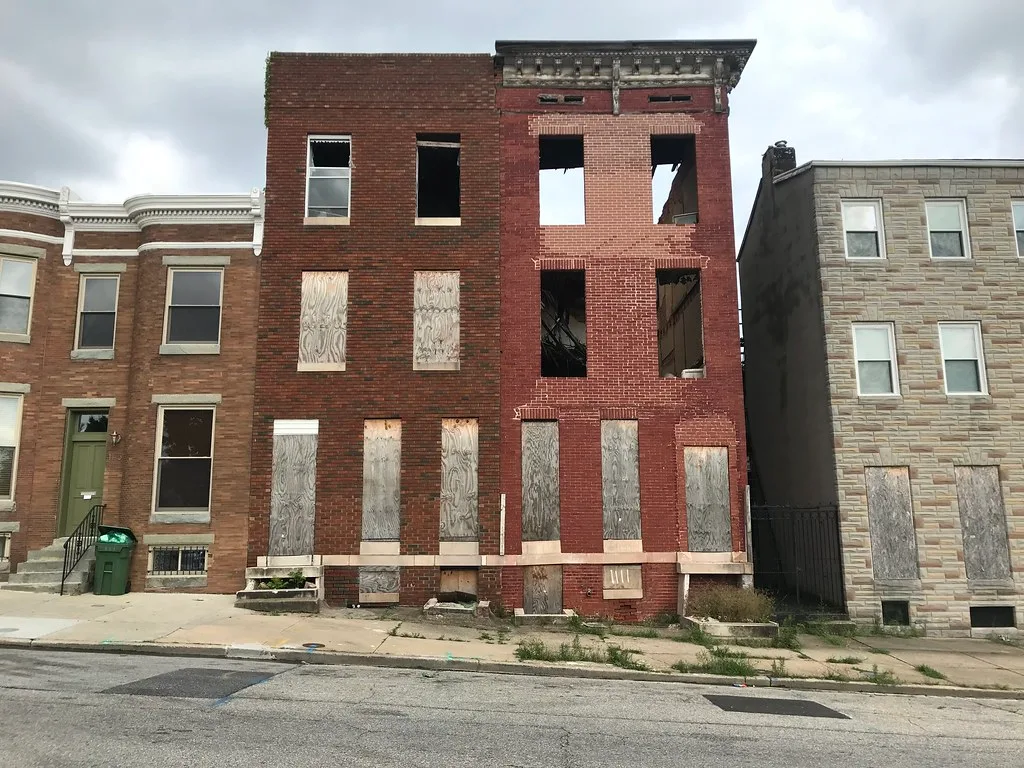 Deux façades de brique abandonnées avec fenêtres béantes et panneaux aux ouvertures basses.