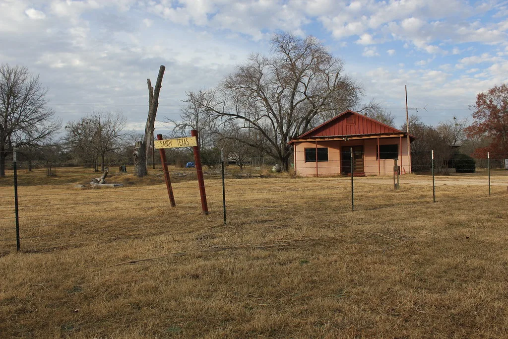 Former post office in Sandy, Texas, a small building behind a fence.