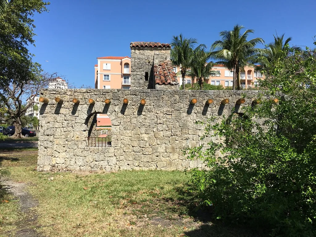Murs de pierre sans toit avec une cheminée et des ouvertures vides devant des palmiers.