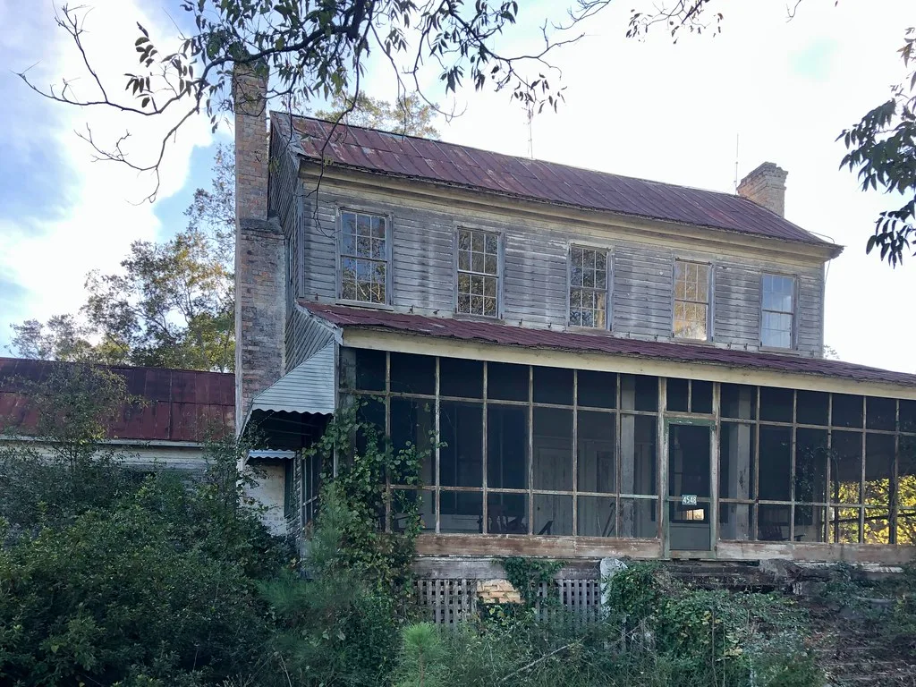 Old wooden house with a long decaying veranda and rusty roof.