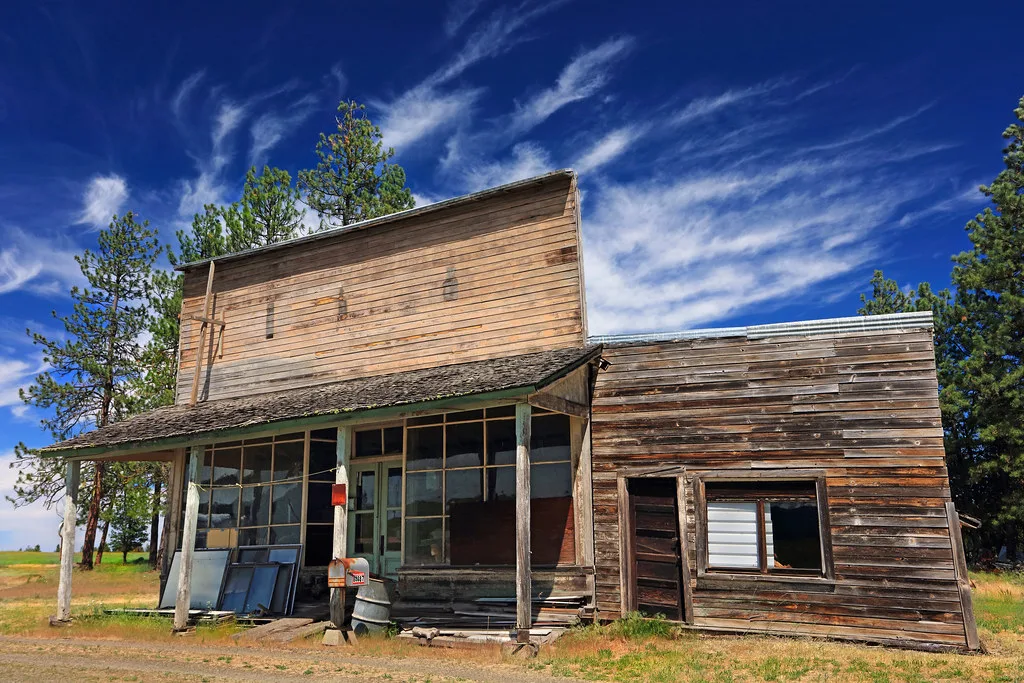 Old wooden shop with deteriorated windows and a damaged porch.