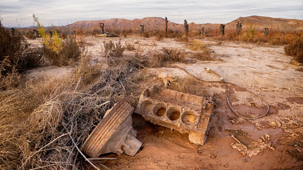 Slab remains and masonry blocks on abandoned ground covered in dry weeds.