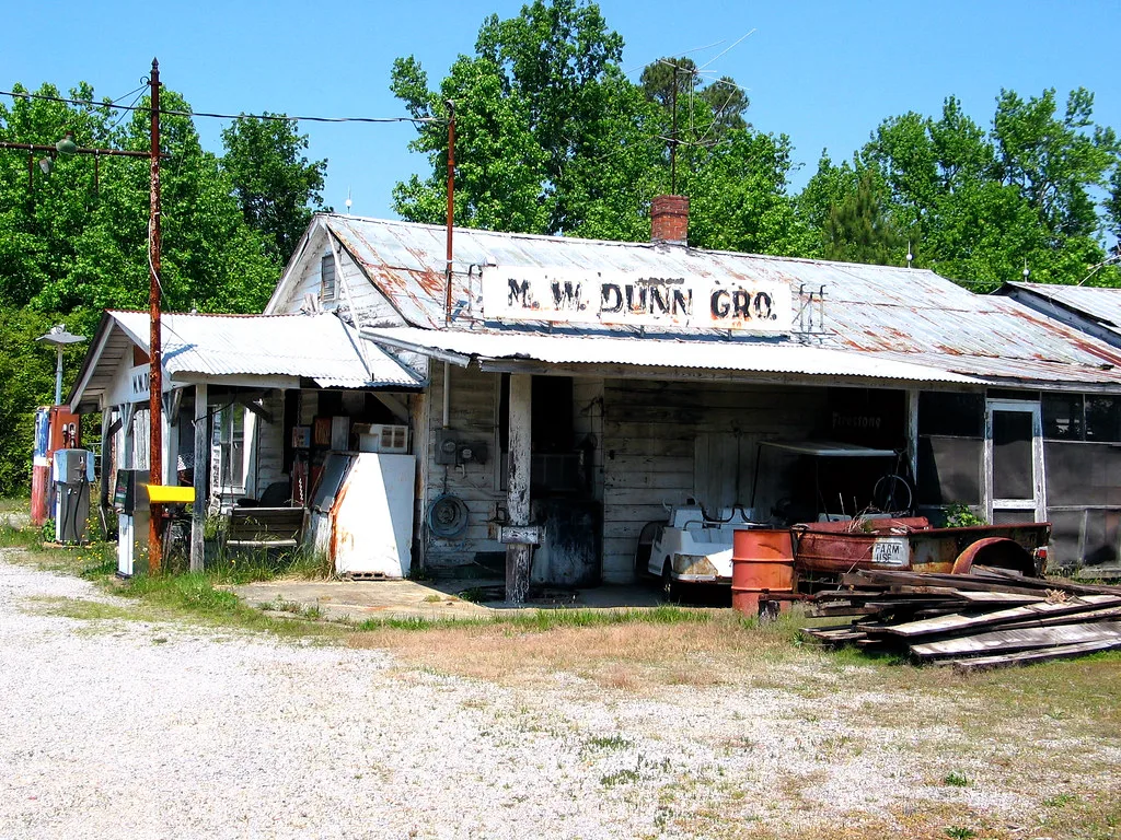 Ancien magasin de bois à toit rouillé avec du matériel ancien sous l’auvent.