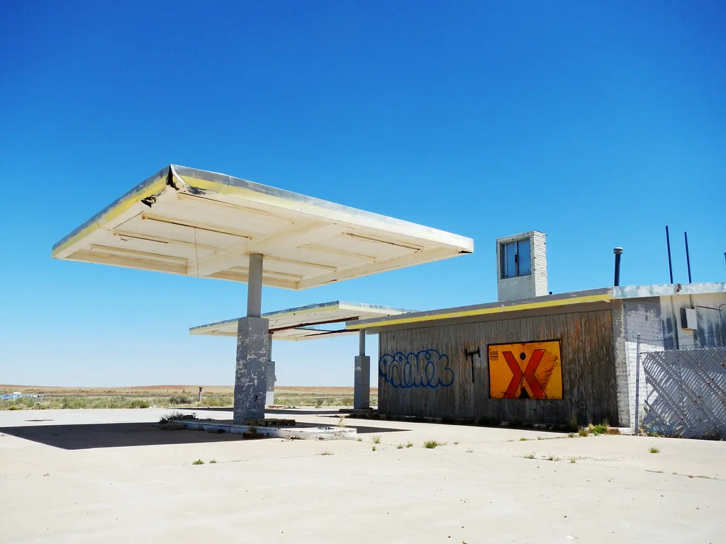Station-service abandonnée aux auvents vides et au bâtiment barricadé couvert de graffitis.