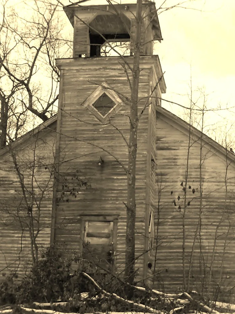 Ancienne église en bois à porte condamnée et clocher abîmé derrière les branches.