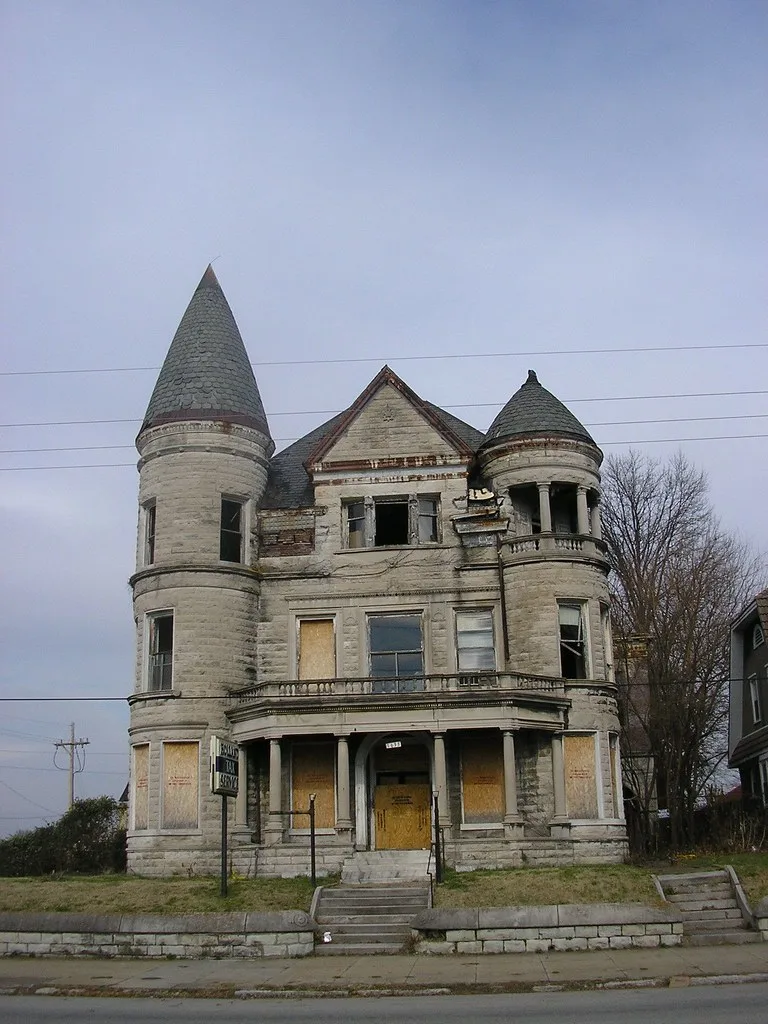 Stone house with two turrets, broken windows and sealed lower openings.