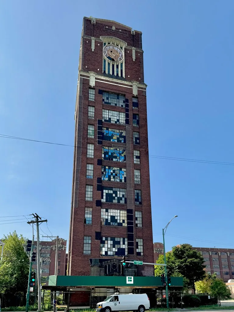 Brick industrial clock tower with long rows of broken windows.