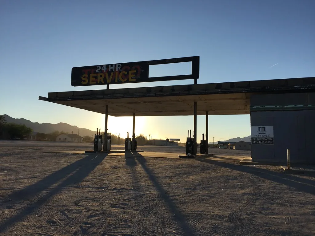 Former petrol station with sealed openings and an incomplete sign in low sunlight.