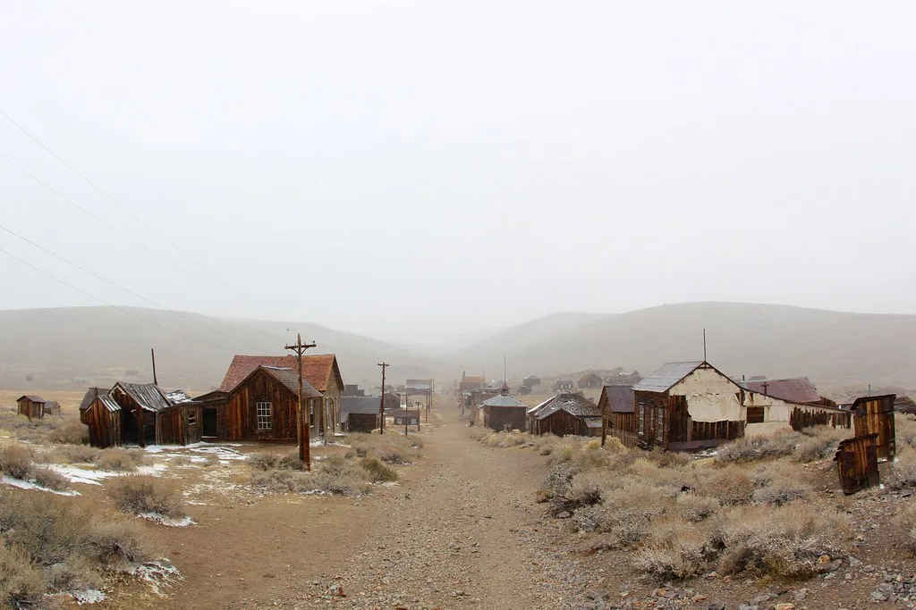 Dirt street lined with derelict wooden houses in a village beneath mist.