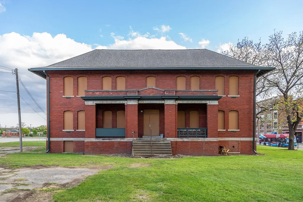 Red brick building with boarded openings in front of a lawn.