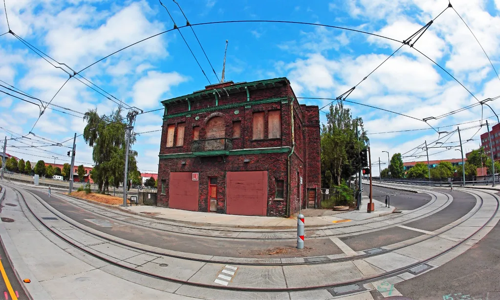 Old red-brick building with boarded openings between two curving tram lines.