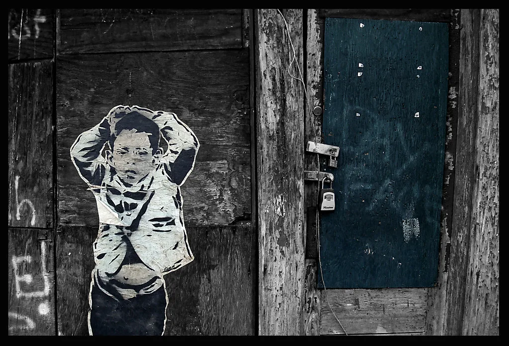 Old boarded blue door beside a painted figure on deteriorated wood.