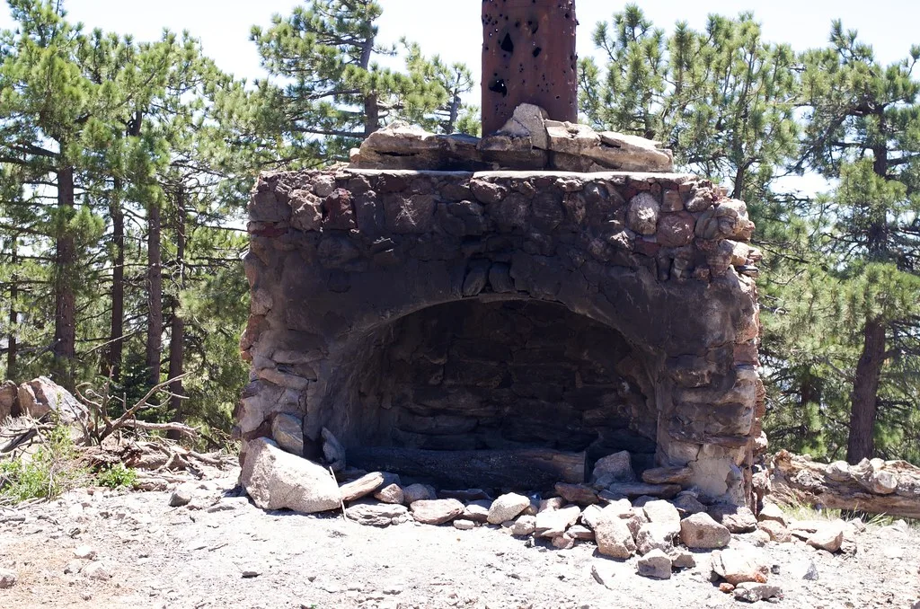 Cheminée de pierre ruinée restée seule parmi des rochers et des pins.