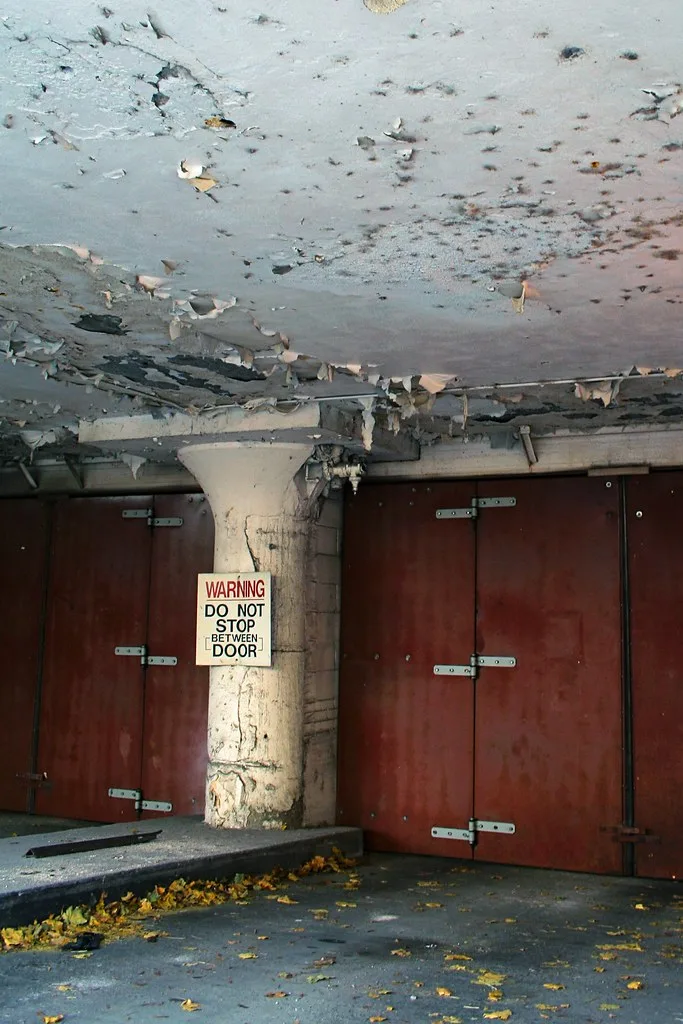 Red doors beneath a peeling ceiling in an abandoned room with scattered debris.