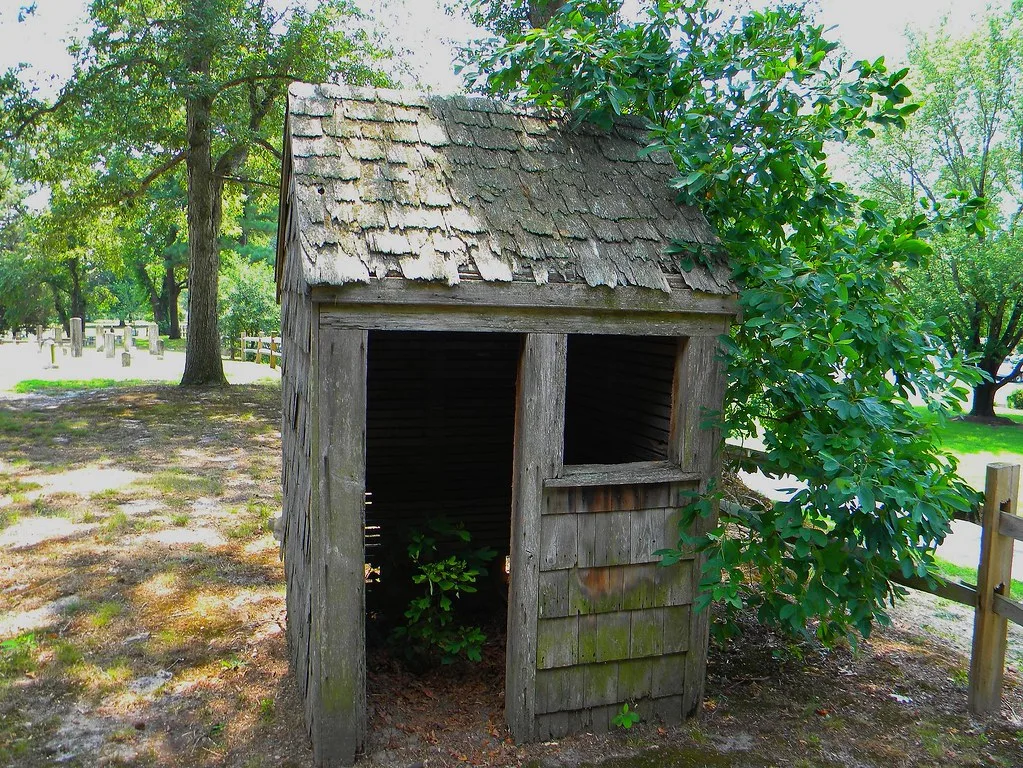 Small weathered wooden hut with open doorway among trees.