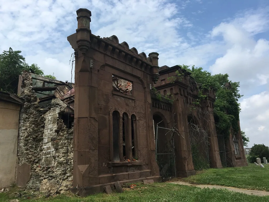 Ornate stone facade of a ruined building with a collapsed roof and vegetation growing in its walls.