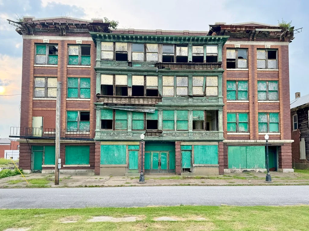 Grand immeuble en briques et décor vert aux fenêtres condamnées.