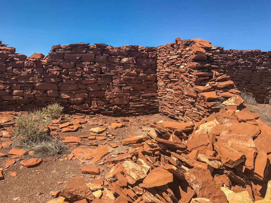 Ruined red stone walls with fallen stones in an open-air room.
