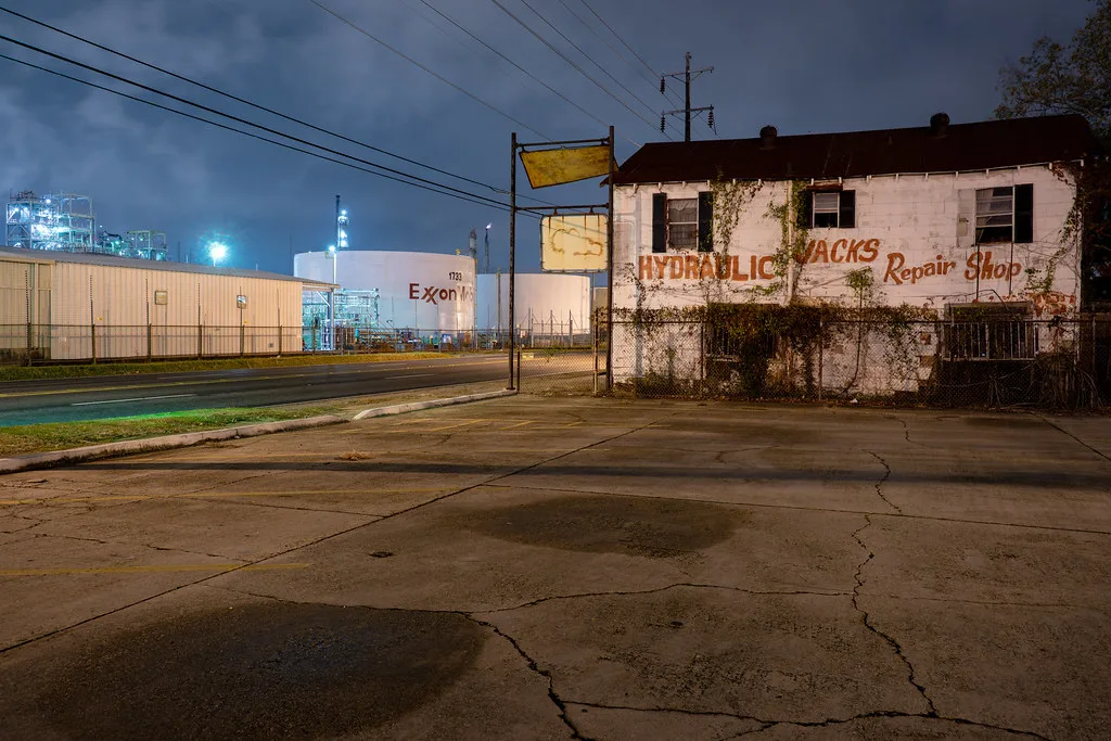 Neglected former hydraulic repair shop with an ivy-covered facade and cracked forecourt at night.