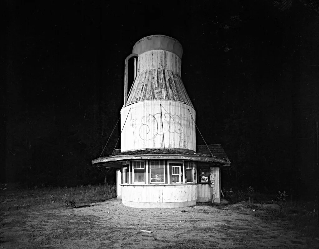 Old milk-can-shaped kiosk photographed at night.