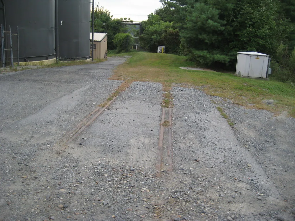 Remnant of rusty railway track disappearing beneath gravel and grass.