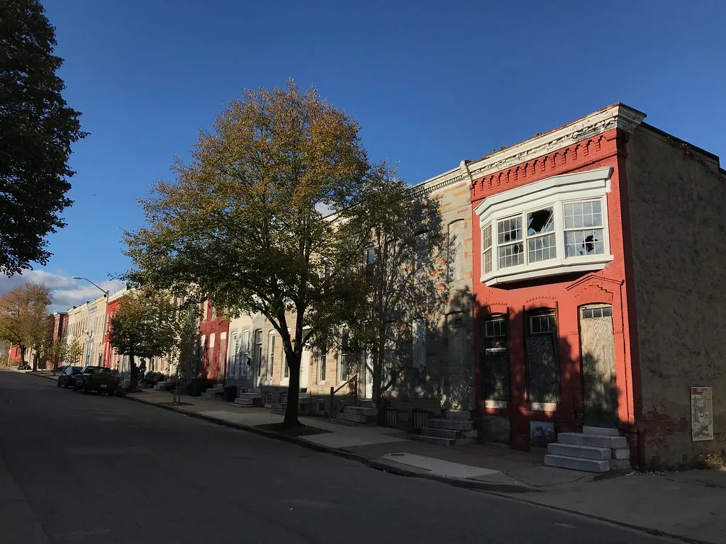 Brick houses with boarded openings and broken windows on a street.