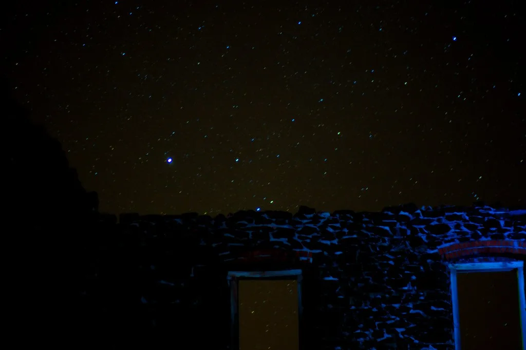 Mur en ruine sans toit avec deux ouvertures rectangulaires éclairées en bleu sous un ciel étoilé.