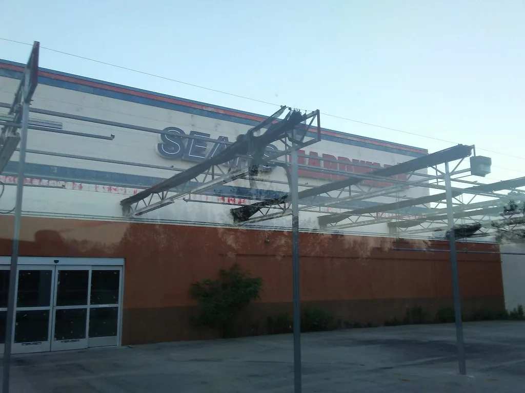 Ancien magasin fermé sous une ossature d’auvent dénudée, avec végétation contre le mur orange.
