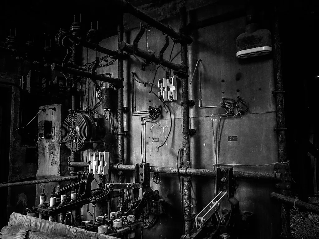 Abandoned electrical panels with porcelain switches and corroded conduits.