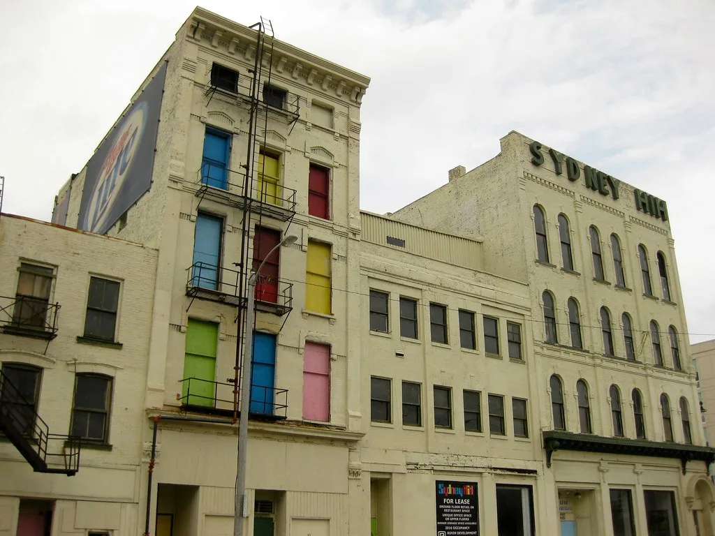 Ancien immeuble clair aux fenêtres condamnées par des panneaux multicolores.