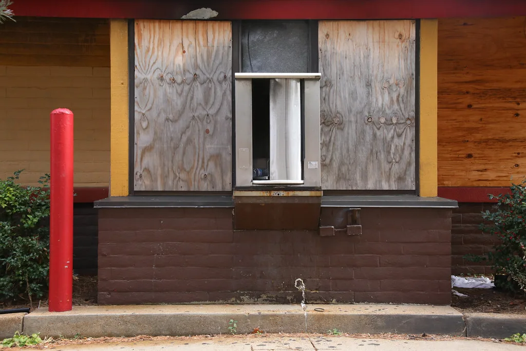 Old service window surrounded by windows boarded with plywood.