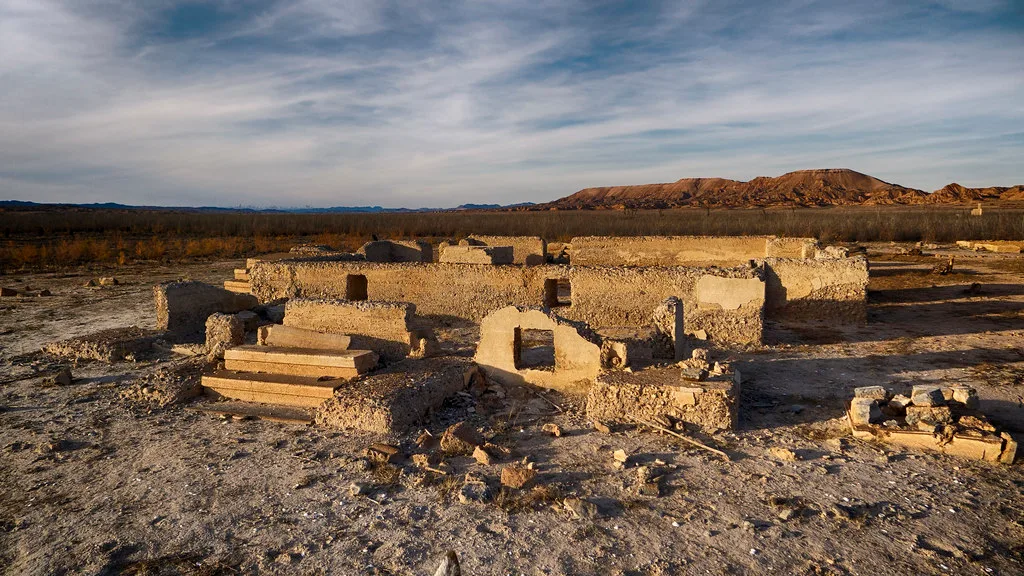 Murs effondrés et petits escaliers de béton d’un site abandonné dans une plaine aride.
