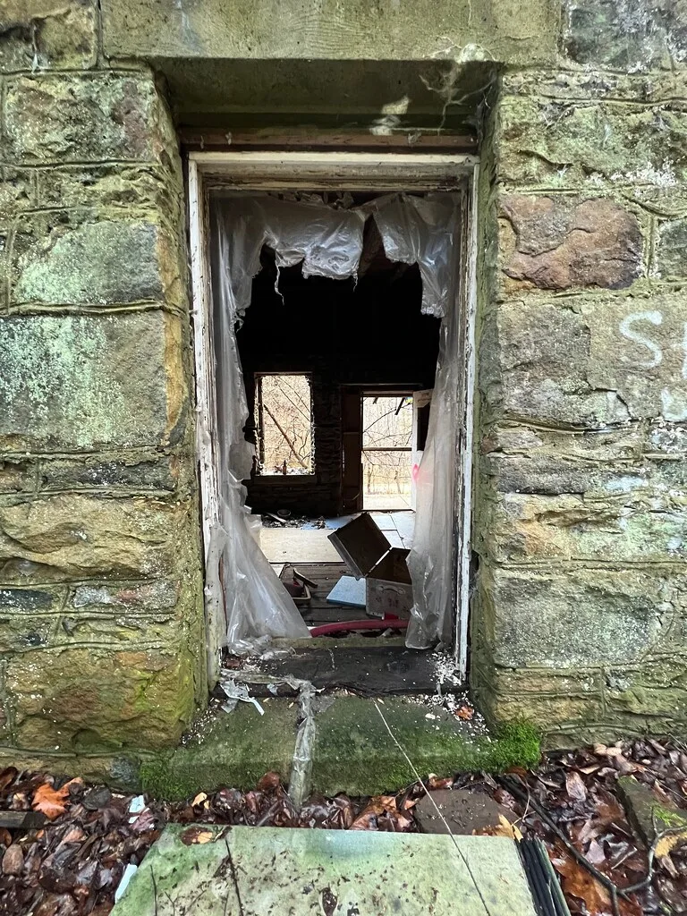Doorless opening in a mossy stone wall leading into a debris-filled abandoned room.