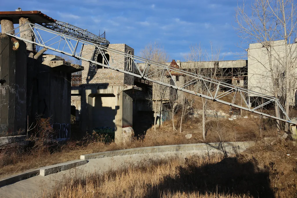 Old industrial structures and a sagging metal walkway amid grass.