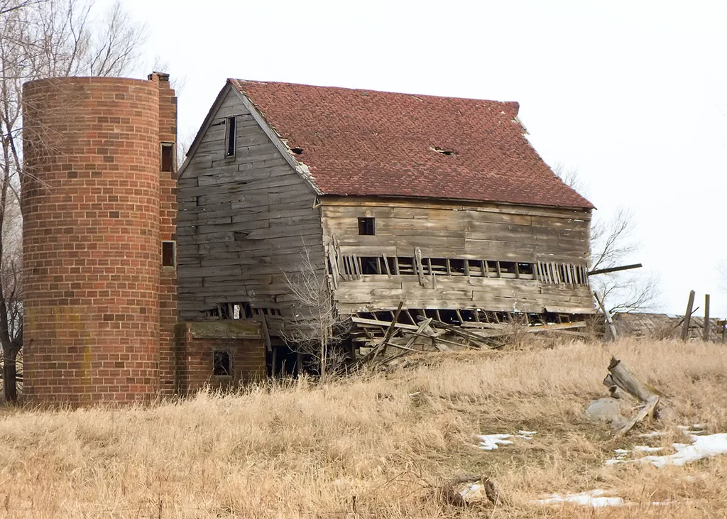 Partly collapsed wooden barn beside a brick silo.