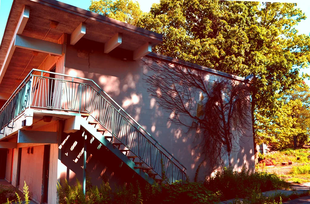 Exterior staircase of an old pink building with overgrown surroundings.