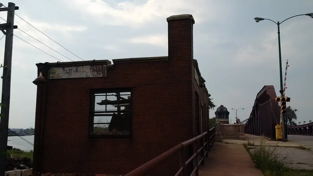Ancien petit bâtiment de briques aux vitres brisées près d’un pont.