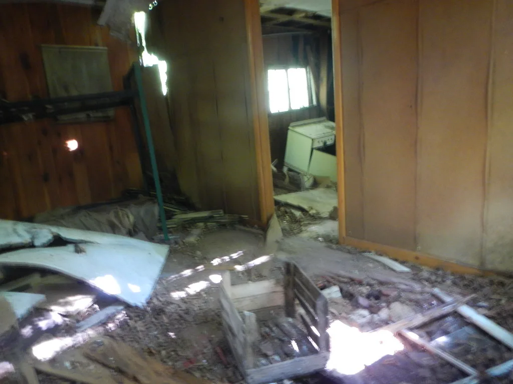 Wooden interior with a collapsed floor and debris in front of an old stove.