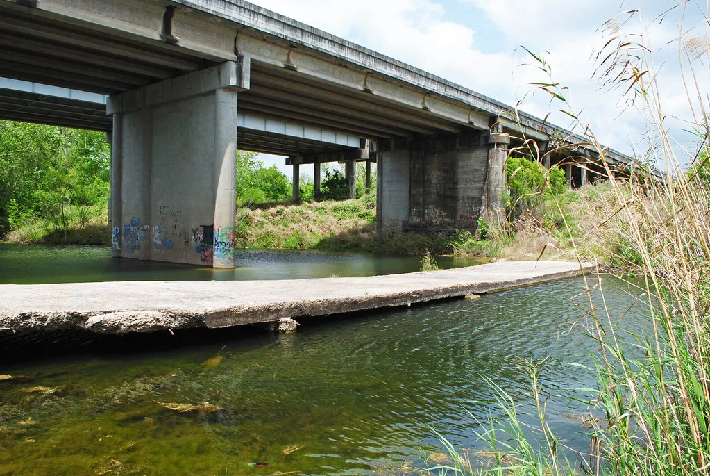 Remnant of a concrete bridge deck in a river beneath a modern bridge.