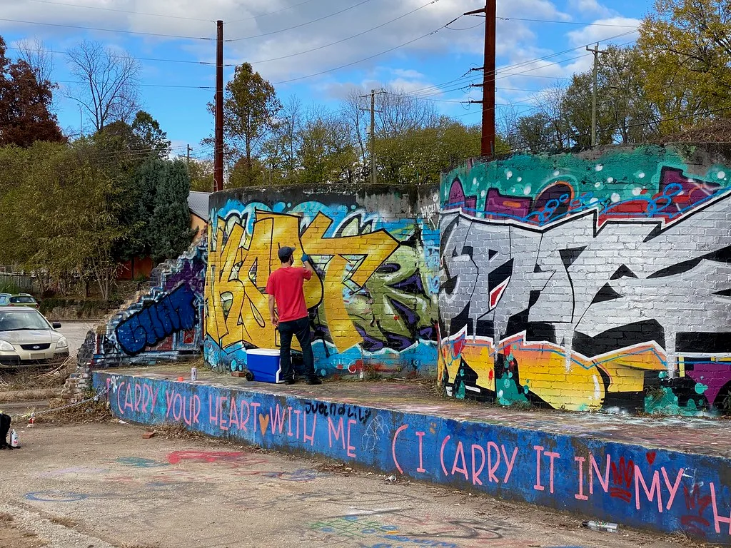 Murs de briques en ruine couverts de graffitis colorés avec une personne peignant la paroi.